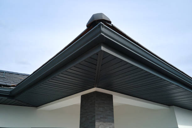 House corner with brown metal planks siding and roof with steel gutter rain system. Roofing, construction, drainage pipes installation.